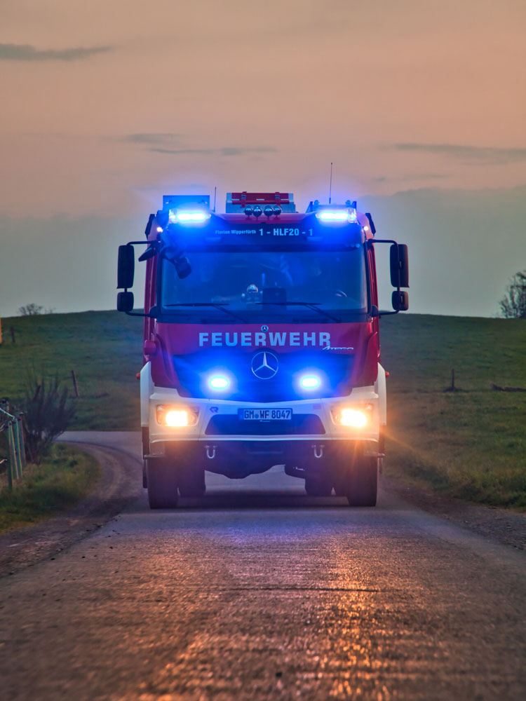 Feuerwehrauto mit Blaulicht auf Straße bei Dämmerung